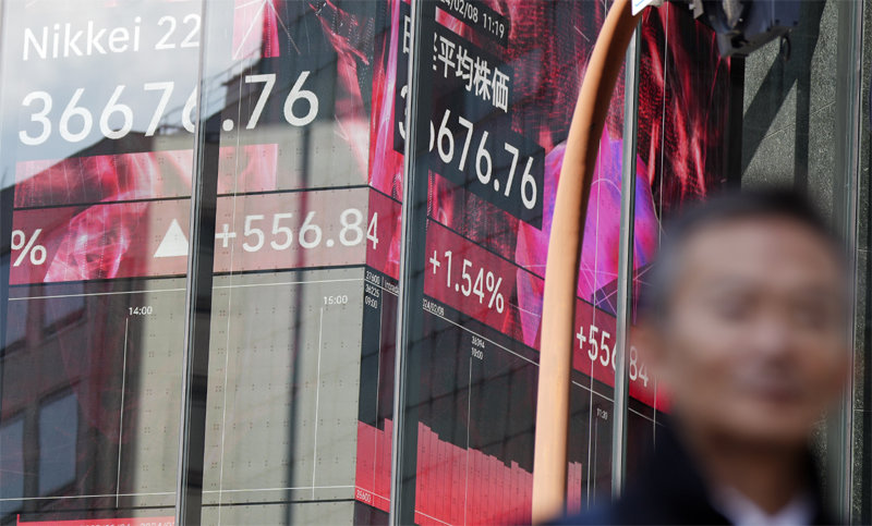 8일 일본 도쿄의 한 증권사 앞에서 한 행인이 닛케이평균주가를 보여주는 전광판 앞을 지나가고 있다. 이날 닛케이평균주가는 34년 만에 최고치를 또 경신했다. 도쿄=AP 뉴시스
