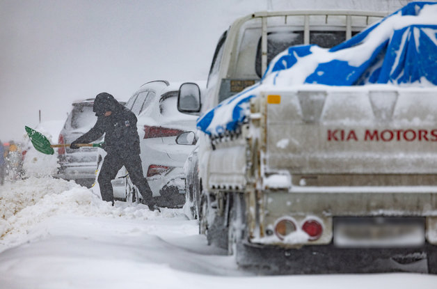 강원 일대에 대설특보가 내려진 21일 오후 강원도 평창군 대관령에서 한 시민이 차량이 빠져나가지 못하자 눈을 치우고 있다. 2024.2.21/뉴스1