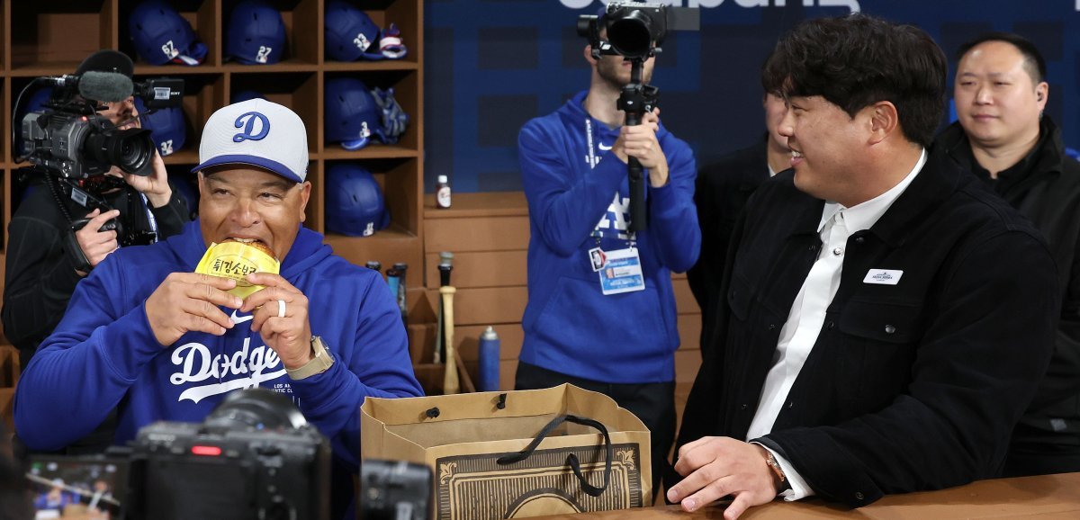 Los Angeles Dodgers manager Dave Roberts (left) is biting into a fried soboro bread gifted by Ryu Hyun-jin ahead of the American professional baseball Major League opening game against San Diego held at Gocheok Sky Dome in Seoul on the 20th.  Newsis