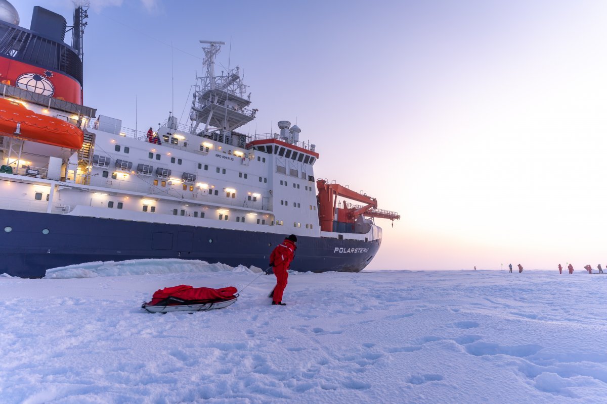 북극해에서 얼음에 갇힌 폴라르슈테른호를 배경으로 원정대원이 장비를 나르고 있다. 멀리 정찰 등 업무를 수행하는 대원들이 보인다. 익스피디아
