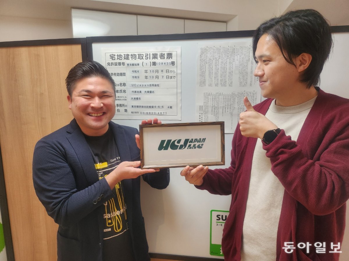 일본 부동산사무소 UC JAPAN의 현판을 들고 있는 김형식 씨(오른쪽)와 그의 동업자 오완 유우시 씨.