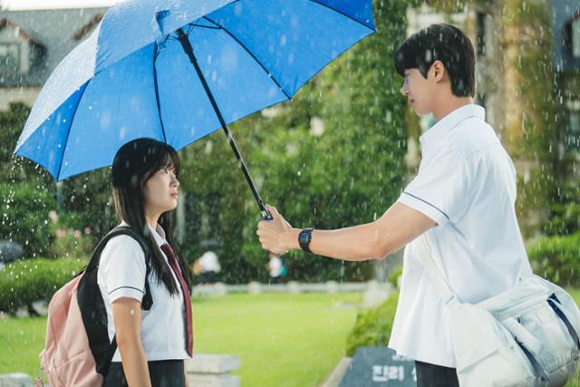 tvN 드라마 ‘선재 업고 튀어’에서 고등학생 남주인공 류선재(변우석·오른쪽)가 파란색 우산을 씌워주자, 여주인공 임솔(김혜윤)이
 선재를 애틋하게 바라보고 있다. 두 사람은 비가 오는 날이면 돌아가며 서로에게 우산을 씌워준다. tvN 제공