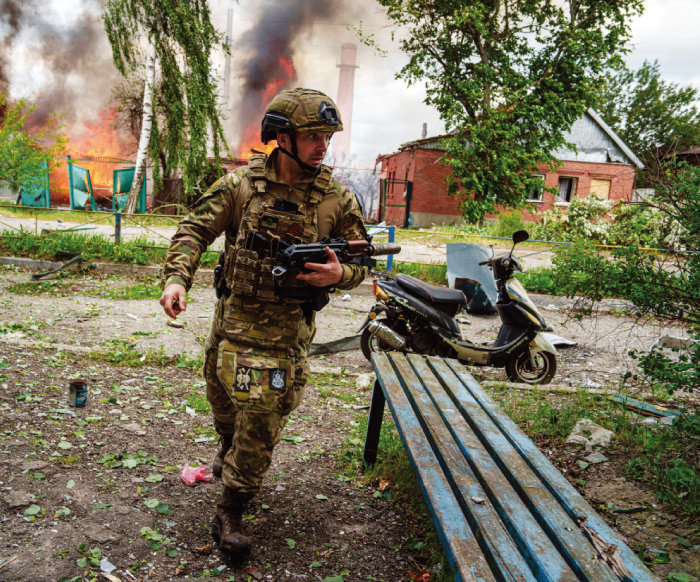 5월 11일(현지 시간) 우크라이나 북동부 하르키우주 보우찬스크에서 한 우크라이나군이 러시아군의 공습으로 불타는 건물을 뒤로한 채 이동하고 있다. [뉴시스]