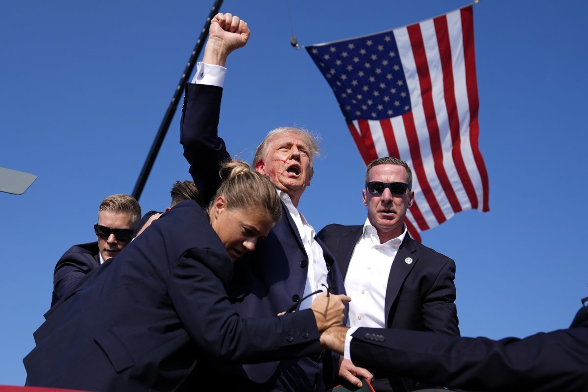 Trump gives a fist bump to supporters as he walks down the podium after being shot. An American flag is visible behind him, hanging from a crane. (AP Photo/Evan Vucci)