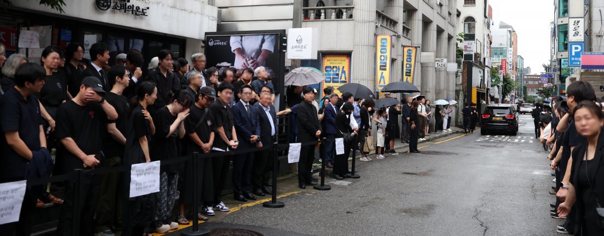 24일 오전 서울 종로구 대학로의 옛 ‘학전’ 소극장 앞길에서 고 김민기의 운구차가 장지를 향해 출발하자 노제에 참석한 사람들이 눈물을 훔치고 있다. 김민기는 참석자들이 불러주는 ‘아침이슬’을 들으며 떠났다. 뉴스1