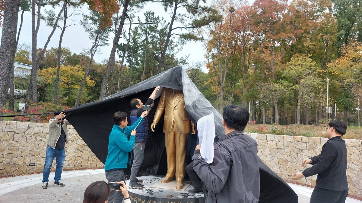 영남대 민주동문회 회원들이 10일 영남대에 건립된 박정희 전 대통령 동상에 달걀과 밀가루를 뿌린 뒤 검은 천을 덮고 있다.(영남대 민주동문회 제공)