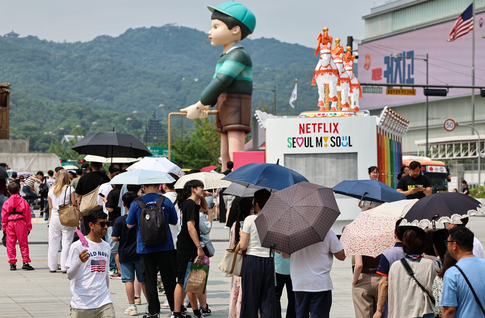 서울 종로구 광화문광장에 마련된 넷플릭스 오징어 게임 체험존에 관광객들이 양산을 쓰고 대기하고 있다. 2025.7.4/뉴스1