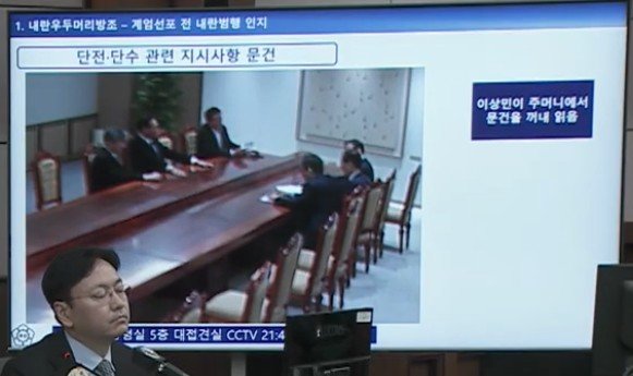 서울중앙지법 형사합의33부(부장판사 이진관) 심리로 열린 한덕수 전 국무총리 2차 공판에서 특검이 제시한 12·3 비상계엄 당일 대통령실 폐쇄회로(CC)TV 영상 화면에 이상민 전 행정안전부 장관이 양복 재킷 안주머니에서 문건을 꺼내 내용을 확인하는 모습이 재생되고 있다. 특검은 윤석열 전 대통령의 언론사 단전·단수 지시가 담긴 문건이라고 주장했다. 법원 공판 중계 화면 캡처