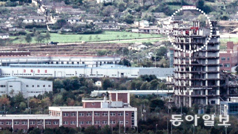 해체되는 개성공단 종합지원센터 14일 경기 파주시 파평산에서 바라본 개성공단 내 종합지원센터(오른쪽 높은 건물) 옥상에서 굴착기(점선 안)가 건물 해체 작업을 하는 모습이 포착됐다. 이날 통일부는 ‘개성공단의 발전적 정상화’를 위한 조직 개편 방안을 발표했다. 파주=홍진환 기자 jean@donga.com