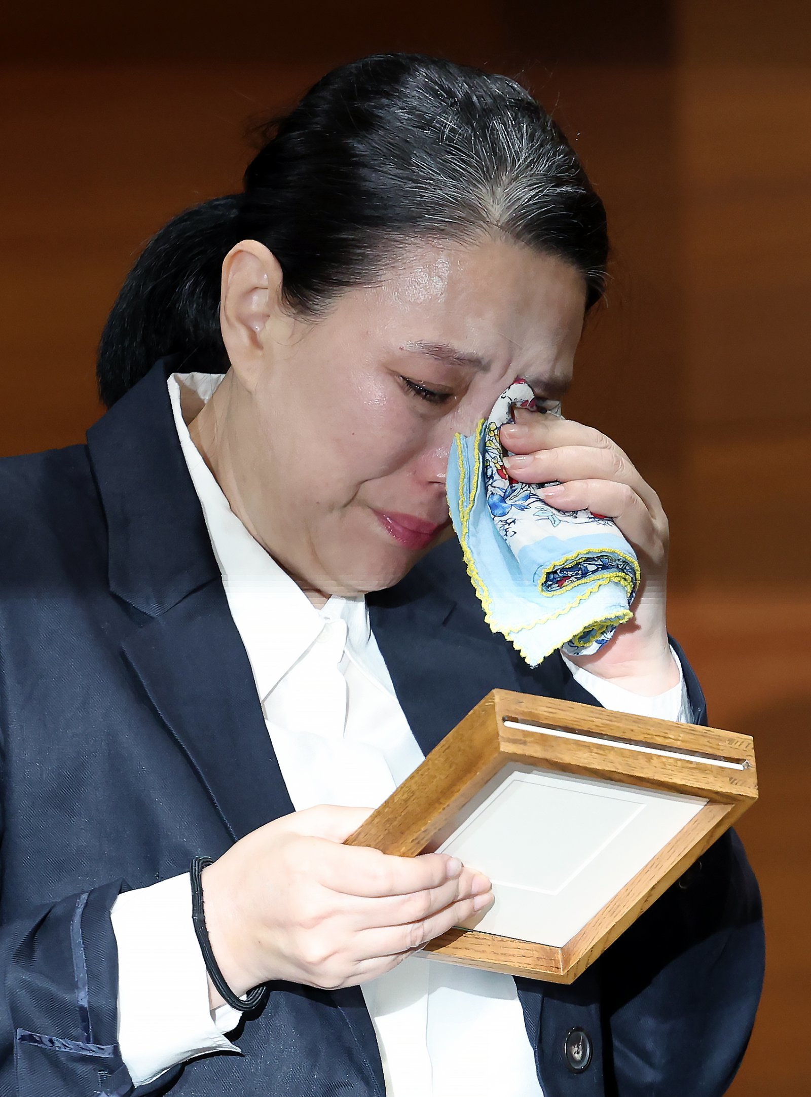 직장 내 괴롭힘을 호소하며 스스로 목숨을 끊은 MBC 기상캐스터 오요안나 씨의 어머니 장연미 씨가 15일 오전 서울시 마포구 상암동 MBC 상암사옥 골든마우스홀에서 열린 MBC-고 오요안나 유족 기자회견에서 안형준 MBC 사장에게 받은 고인의 명예 사원증을 바라보며 눈물을 훔치고 있다. 뉴스1