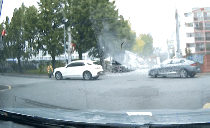 골목길 사거리에서 자동차 고사를 지내는 한 여성. 자차로 추정되는 흰색 제네시스 차량 주변에 술을 뿌리고 있다. 옆으로는 SUV 차량과 트럭이 아슬아슬 지나고 있다. (출처=보배드림 캡처)