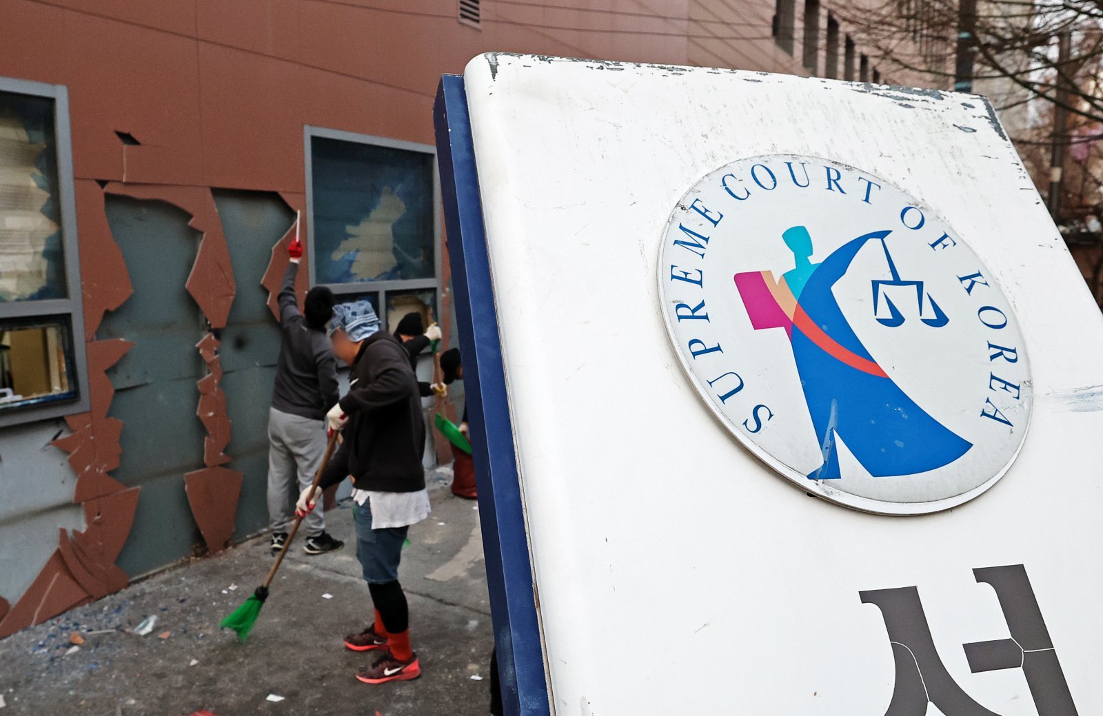 19일 오후 윤석열 대통령 지지자들의 폭력 난입 사태가 발생한 서울 마포구 서울서부지방법원 후문의 기울어진 법원 현판 뒤에서 관계자들이 폐기물을 치우고 있다. 2025.1.19/뉴스1