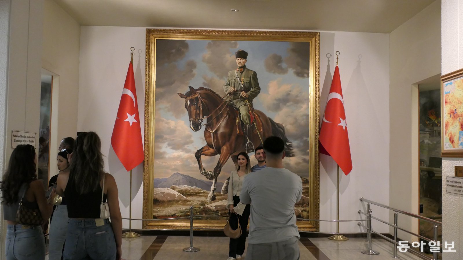 젊은 남녀가 아느트카비르 아타튀르크 박물관에 있는 튀르키예 국부 무스타파 케말 아타튀르크 전신 초상화 앞에서 기념 사진을 찍고 있다.