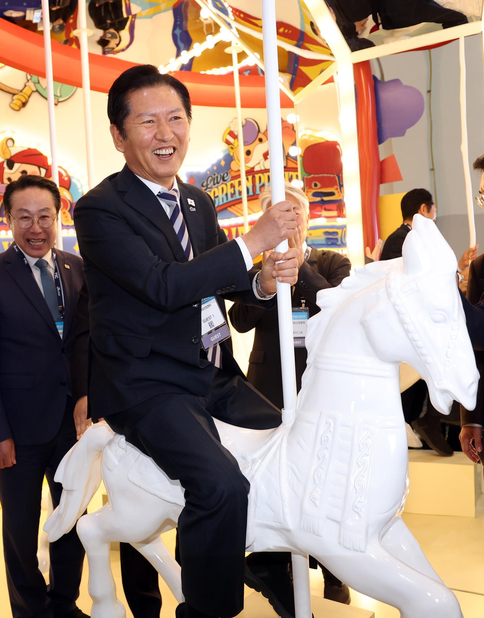 정청래 더불어민주당 대표가 14일 부산 해운대구 벡스코에서 열린 글로벌 게임전시회 ‘지스타 2025’ 행사장을 방문, 게임업체 부스에 마련된 회전목마 포토존에 오르고 있다. 2025.11.14. 뉴시스