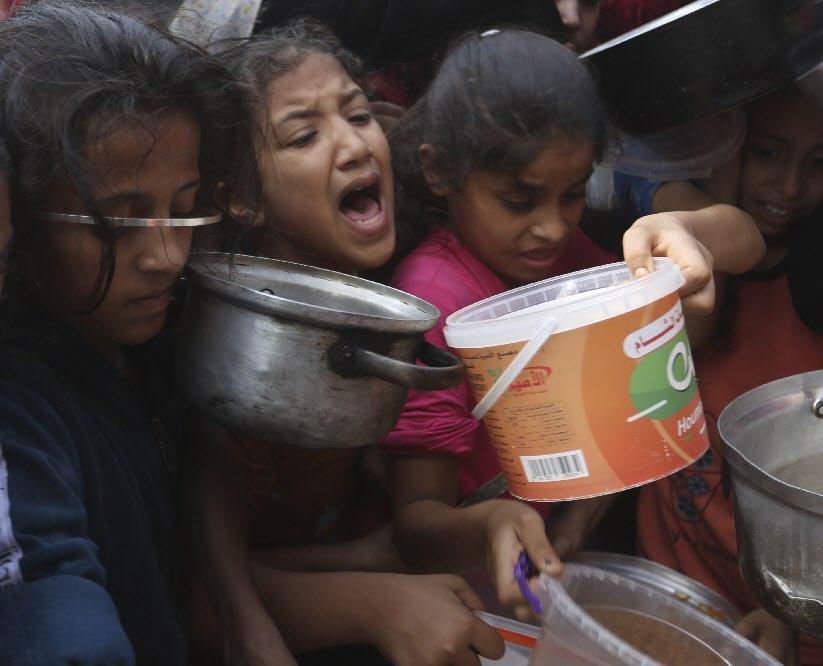 지난해 11월 이집트와 국경을 맞댄 팔레스타인 가자지구 남부 라파에서 팔레스타인 어린이들이 음식을 배급받기 위해 서로 앞다퉈 냄비와 플라스틱통 등을 내밀고 있다. 라파=AP 뉴시스