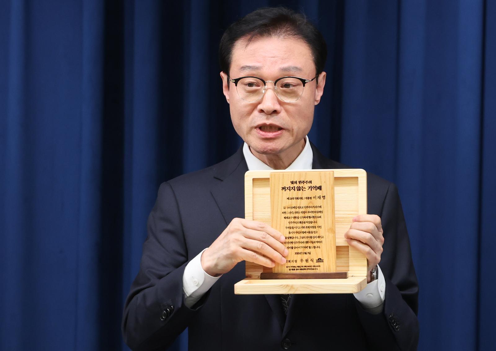 이규연 홍보소통수석이 3일 서울 용산 대통령실 청사에서 열린 5부 요인 초청 오찬 관련 브리핑에서 ‘빛의 민주주의 꺼지지 않는 기억패’를 들어 보이고 있다. 이재명 대통령은 이날 오찬에서 우원식 국회의장으로부터 지난해 12월 3일 계엄군에 의해 부서졌던 국회 집기들을 재활용해 만든 ‘기억패’를 전달받았다. 뉴스1