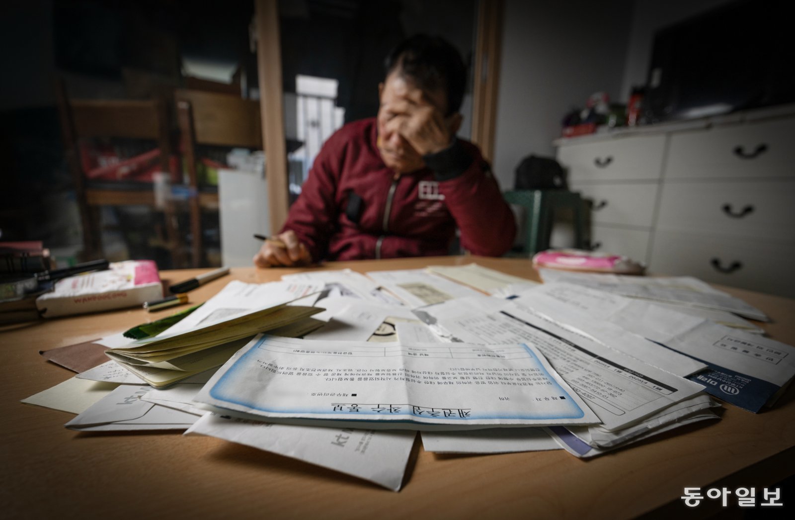 이달 3일 경남 진주시의 한 임대주택에서 문영식 씨가 채권추심착수통보서 등이 어지럽게 펼쳐져 있는 서류를 보며 얼굴을 감싸고 있다. 영식은 2년 전 겨울 자신을 ‘아빠’라고 부르는 30대 여성에게 휴대전화 개통을 강제당하며 통장을 넘겨주게 됐다.