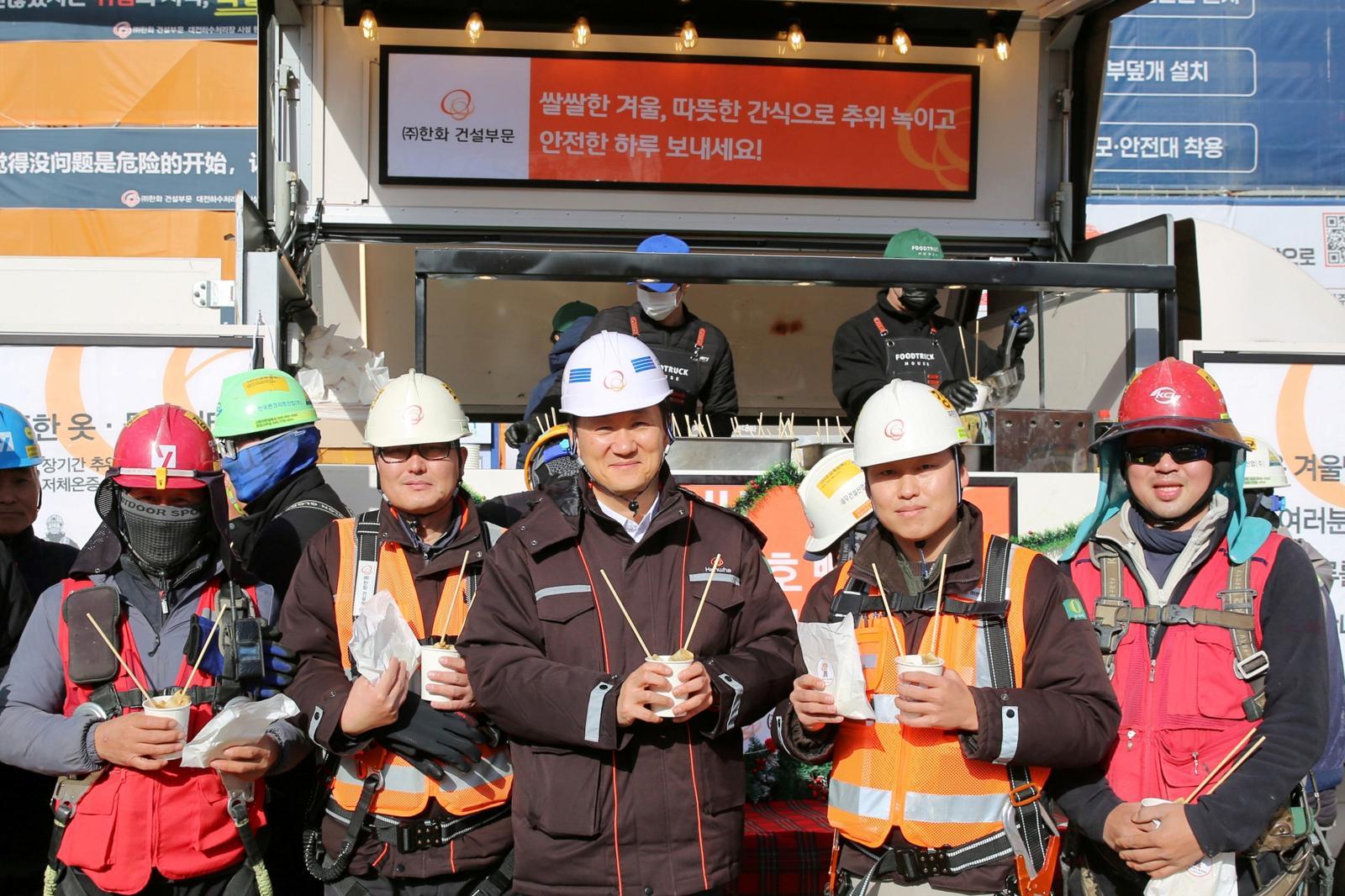 김우석 한화 건설부문 대표이사(가운데)가 건설현장 근로자들과 함께 ‘찾아가는 겨울간식차’의 호빵과 어묵을 즐기고 있다.
