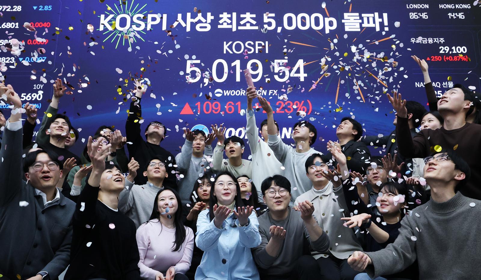 한국 증시가 사상 처음으로 ‘코스피 5000’ 쾌거를 달성한 22일 서울 중구 우리은행 본점 딜링룸에서 직원들이 장중 최고가가 찍힌 전광판을 배경으로 코스피 5000 돌파를 축하하고 있다. 2026.1.22 뉴스1