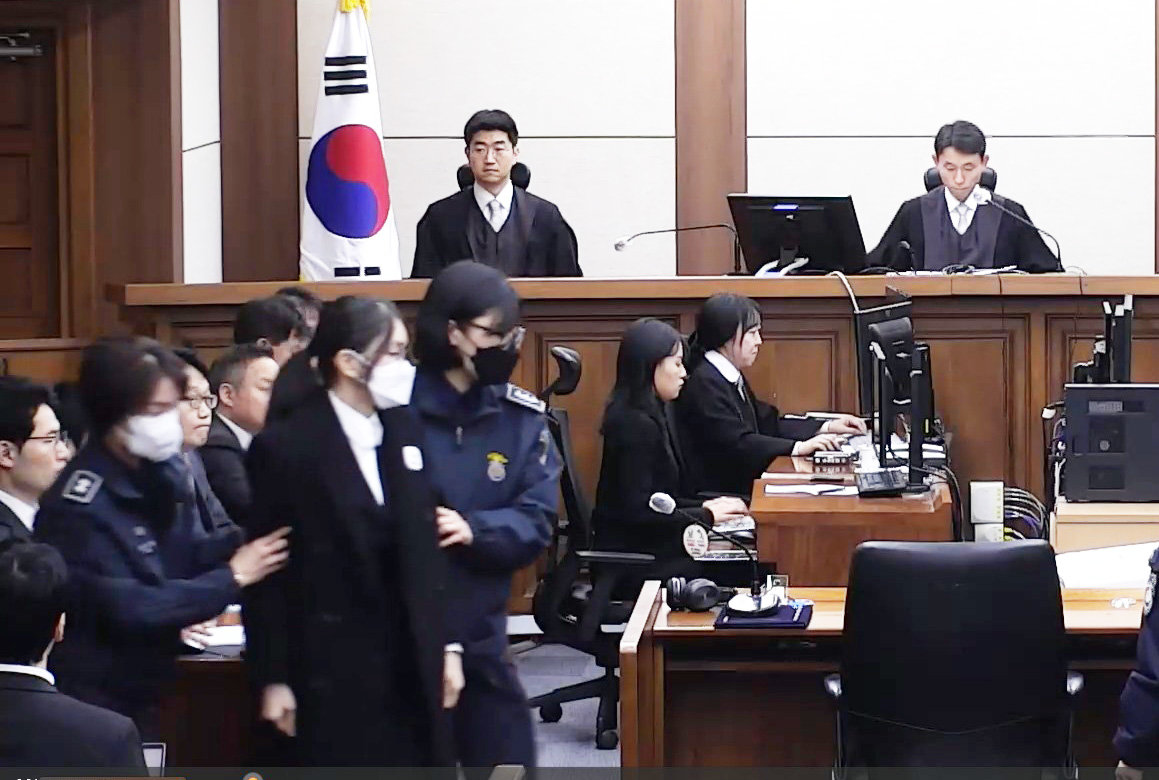 김건희, 마스크 쓰고 법정 출석
28일 오후 서울중앙지법에서 열린 김건희 여사 1심 선고 공판에서 김 여사가 흰색 마스크를 쓴 채 교도관의 부축을 받으며 법정에 들어서고 있다. 재판부는 김 여사가 통일교 측으로부터 청탁과 함께 샤넬 가방 1개와 그라프 다이아몬드 목걸이를 받은 혐의를 유죄로 판단하고 징역 1년 8개월의 실형을 선고했다. 전직 대통령 부부가 동시에 실형 선고를 받은 건 헌정 사상 처음이다. 서울중앙지법 재판 중계 화면 캡처