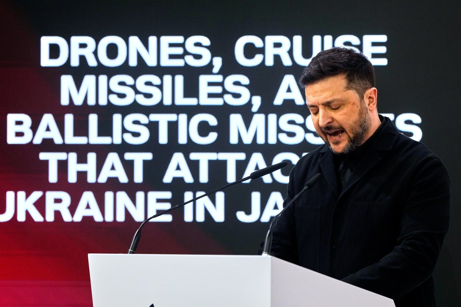 볼로디미르 젤렌스키 우크라이나 대통령이 14일 독일 뮌헨안보회의에서 연설하고 있다. 뒤로 러시아 드론과 크루즈 미사일 등이 우크라이나를 공격한다는 문구가 보인다.2026.02.14 뮌헨=AP 뉴시스