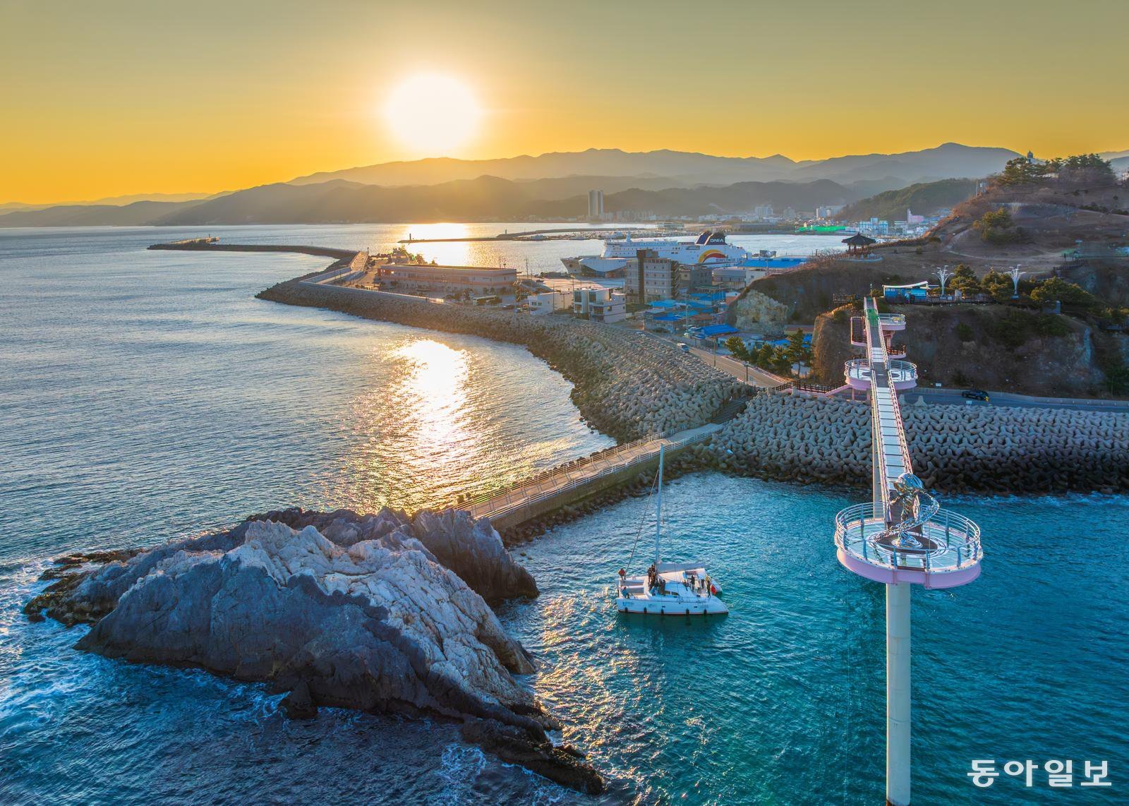 경북 울진 후포항에서 출발한 요트 승객들이 노을이 지는 바다에서 등기산 스카이워크와 갓바위를 감상하고 있다.