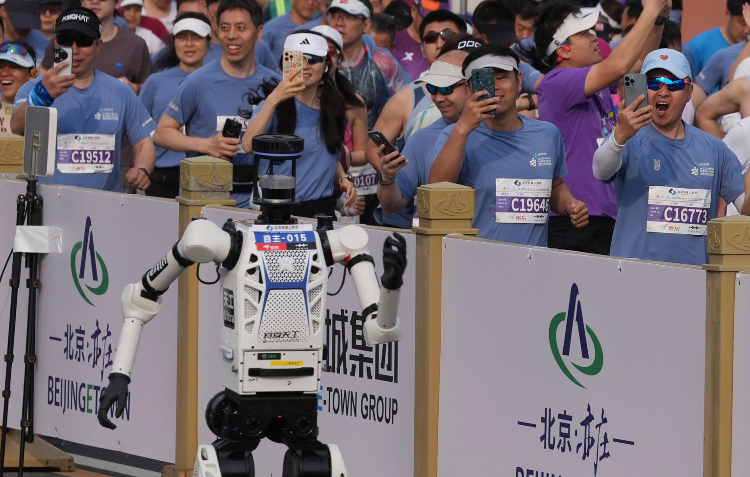 19일 중국 베이징에서 열린 ‘2026 휴머노이드 로봇 하프 마라톤 대회’에서 아너사의 자율주행 휴머노이드 로봇 산뎬이 50분26초 만에 완주하며 우승했다(위쪽 사진). 우간다의 육상 선수 제이컵 키플리모가 올 3월 리스본에서 세운 세계신기록(57분20초)보다 약 7분 빠르다. 이날 대회에는 1만여 명의 마라토너와 로봇 105대가 출전해 나란히 뛰었다. 베이징=AP 뉴시스