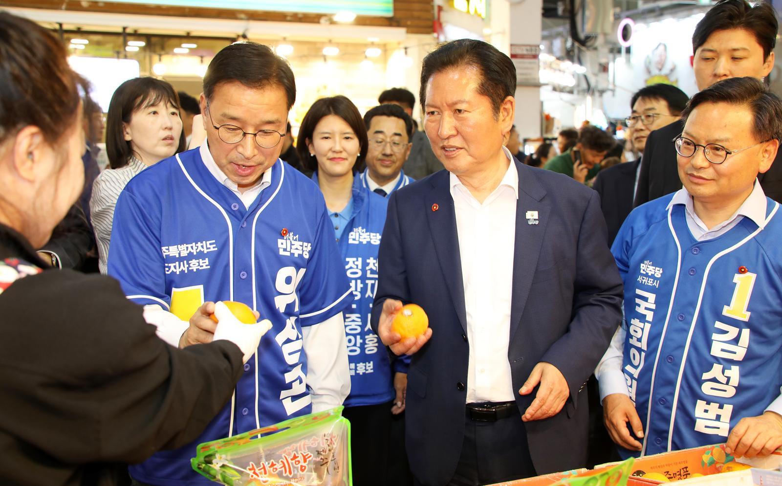 정청래 더불어민주당 대표가 15일 오후 서귀포매일올레시장에서 위성곤 민주당 제주도지사 후보, 김성범 서귀포시 국회의원 보궐선거 후보와 함께 귤을 들고 있다. 2026.5.15 ⓒ 뉴스1