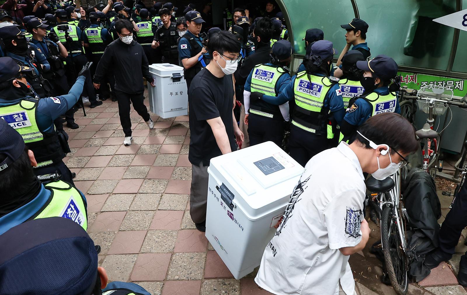 이날 서울 송파구 잠실7동 제2투표소 앞에서 서울시선거관리위원회 관계자들이 투표함 2개를 옮기고 있다. 이 투표소 주변엔 용지 부족에 항의하며 재선거를 요구하는 시위대가 3일 오후부터 진을 치고 투표함 이송을 막아 개표가 지연돼 왔다. 뉴스1