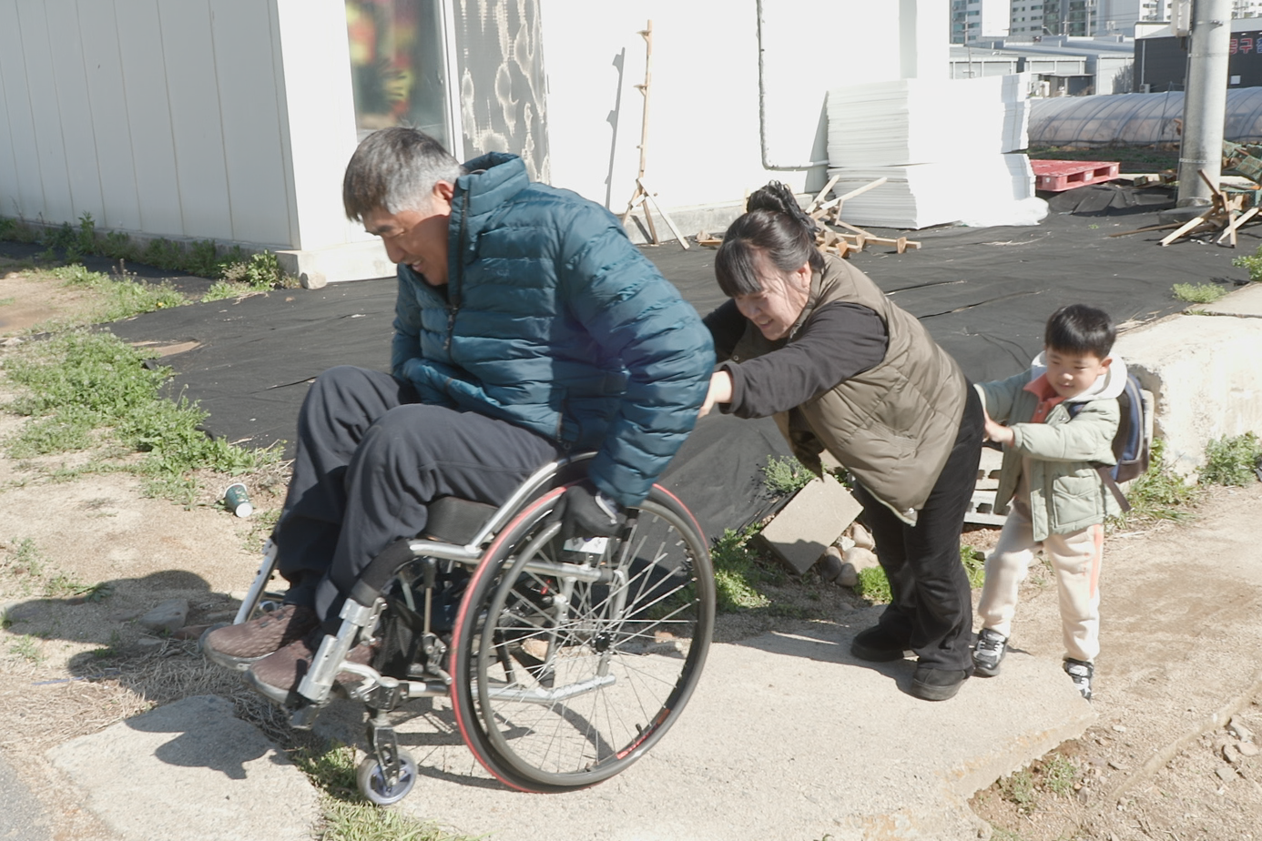 아버지의 휠체어 이동을 돕는 선오와 어머니. 굿네이버스 제공.
