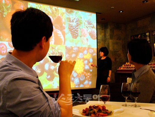 김새길 부원장이 레드 와인을 만드는 다양한 포도 품종을 대형 화면을 통해 보여주는 가운데 스포츠동아 이길상기자(왼쪽)가 이날 설명 들은 와인을 시음하고 있다.