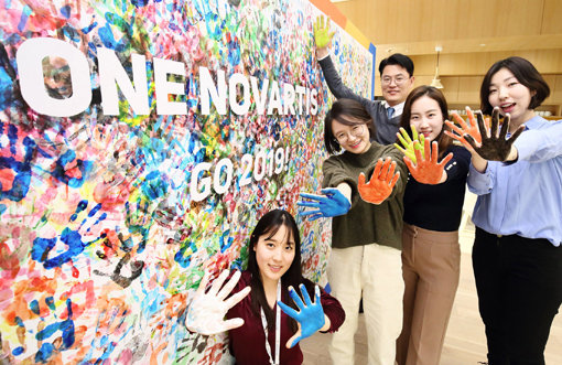 여의도 IFC로 사옥을 이전한 한국노바티스 임직원이 하나된 마음으로 환자와 사회를 위해 헌신하겠다는 의미를 담은 ‘One Novartis’ 슬로건이 새겨진 대형 핸드 프린팅 포토월에서 기념촬영을 하고 있다. 사진제공｜한국노바티스