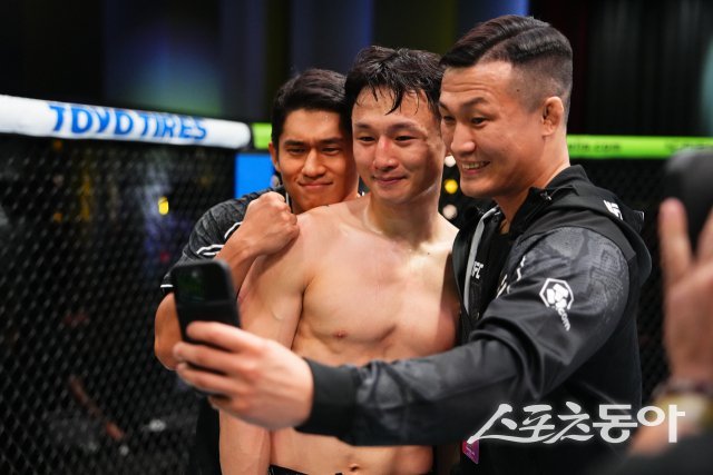 최두호(가운데)가 21일 미국 라스베이거스 UFC에이펙스에서 열린 페더급 경기에서 빌 알지오를 TKO로 제압한 후 코치를 맡은 정찬성(오른쪽)과 사진을 찍으며 기뻐하고 있다. 사진제공 ㅣ UFC