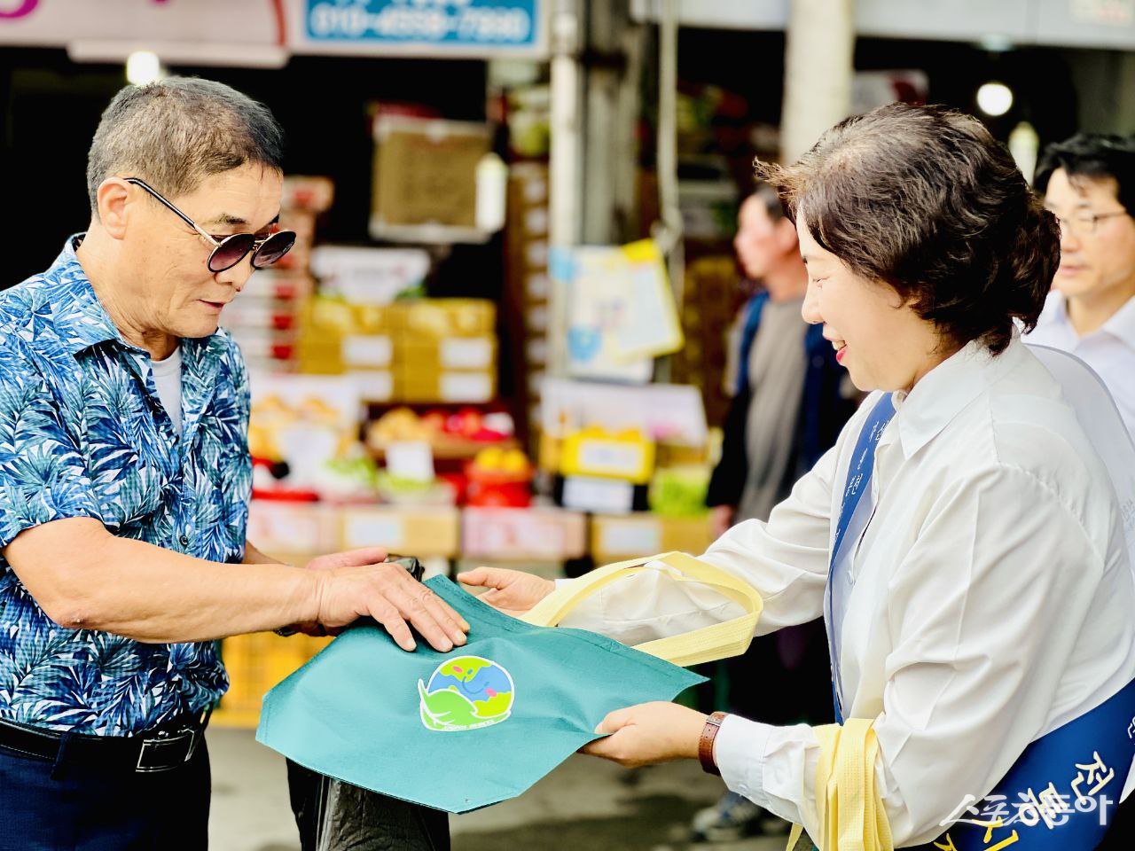 봉사자가 한 시민에게 장바구니를 전하며 시장 이용을 권면하고 있다. (사진제공=신천지자원봉사단 마산지부)