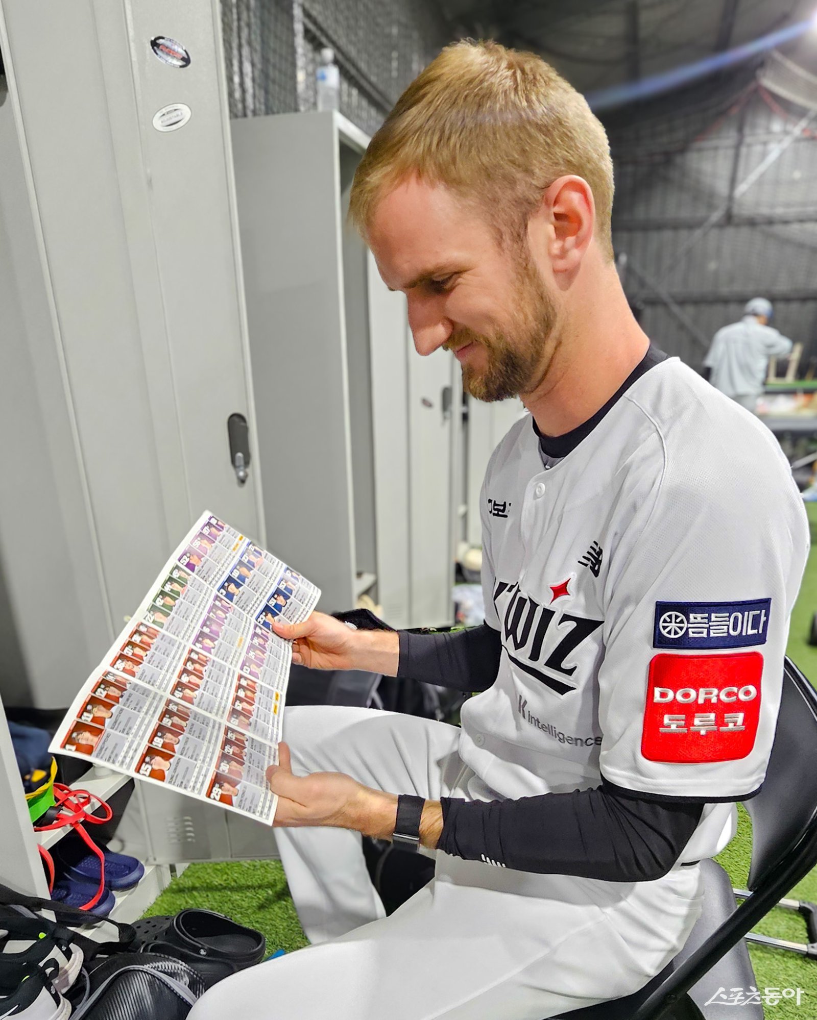 KT 외국인 투수 케일럽 보쉴리가 26일 호주 질롱 베이스볼 센터의 라커룸에 앉아 구단 커뮤니케이션팀 주도로 제작한 선수단 안내 팸플릿을 보고 있다. 함나얀 커뮤니케이션팀 대리, 정민주 마케팅기획팀 매니저가 매년 팸플릿을 직접 기획하고 제작해 한국야구를 알리고 있다. 사진제공|KT 위즈